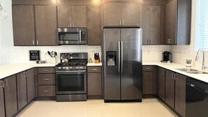 Une cuisine moderne dotée d’appareils électroménagers en acier inoxydable, de meubles de rangement en bois foncé et d’un plan de travail blanc.