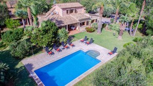 A large swimming pool with lounge chairs and a stone house with a tiled roof. - Villa Joanna (Pollença)