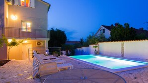 A two-story building with a swimming pool, outdoor seating, and a stone patio.