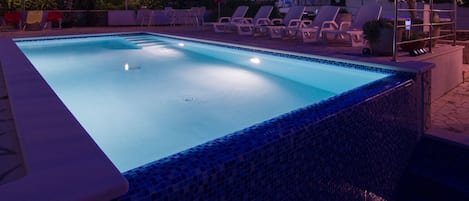 A rectangular swimming pool with a tiled edge, surrounded by lounge chairs and a small deck area.