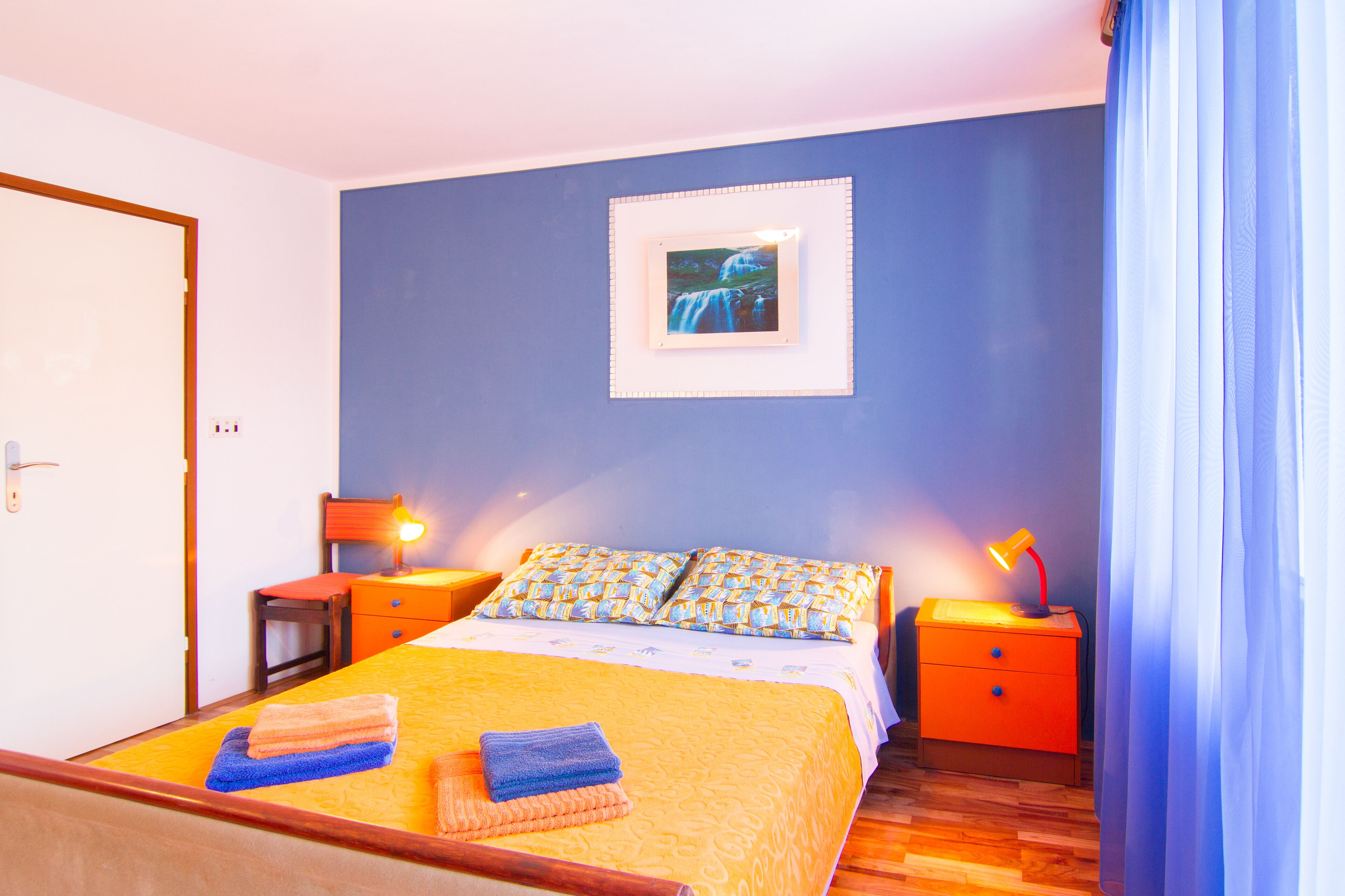 Une chambre à coucher avec un lit, deux tables de chevet, un tableau accroché au mur et une porte.