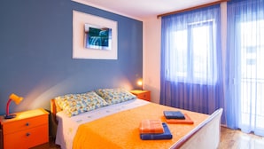 A bedroom with a bed, nightstands, a lamp, a painting, and a window with curtains.