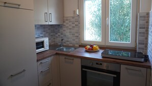 A modern kitchen with white cabinets, a microwave, a sink, and a window with a view of greenery.