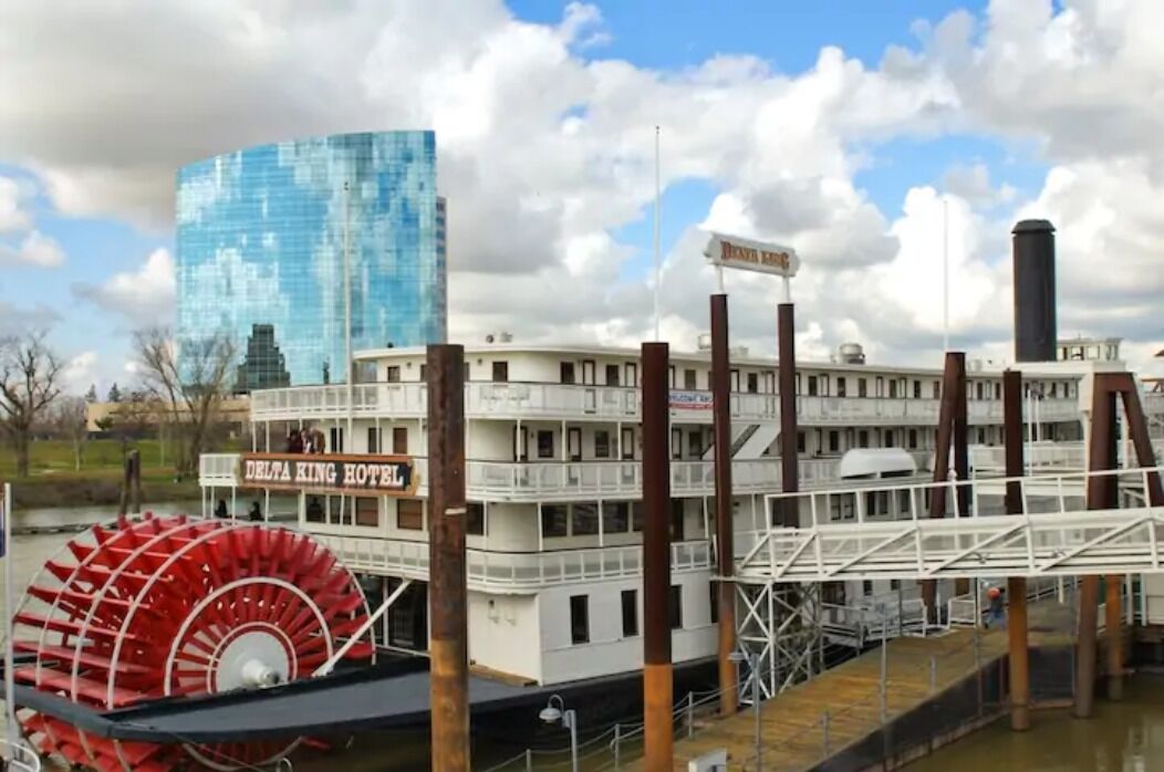 Um hotel em barco de rio com uma grande roda de pás vermelha, fachada branca e um letreiro com a inscrição "DELTA KING HOTEL".