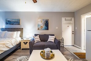 A hotel room with a bed, a sofa, a coffee table with a tray, a painting, and a door with a coat rack. - Private Studio in Carmichael w/Netflix, Disney+ (Sacramento)