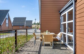 A patio with wicker furniture and a glass door, adjacent to a building with a brown siding exterior.
