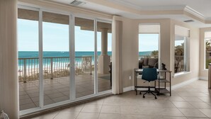 A spacious room with a large sliding glass door leading to a balcony with a view of the beach and ocean.