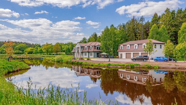 Un cadre paisible au bord d’un lac, avec deux maisons, un ciel dégagé et une étendue d’eau calme qui reflète l’environnement.