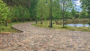 Un sentier pavé de pierres, sinueux, qui traverse un parc arboré et longe un plan d’eau.