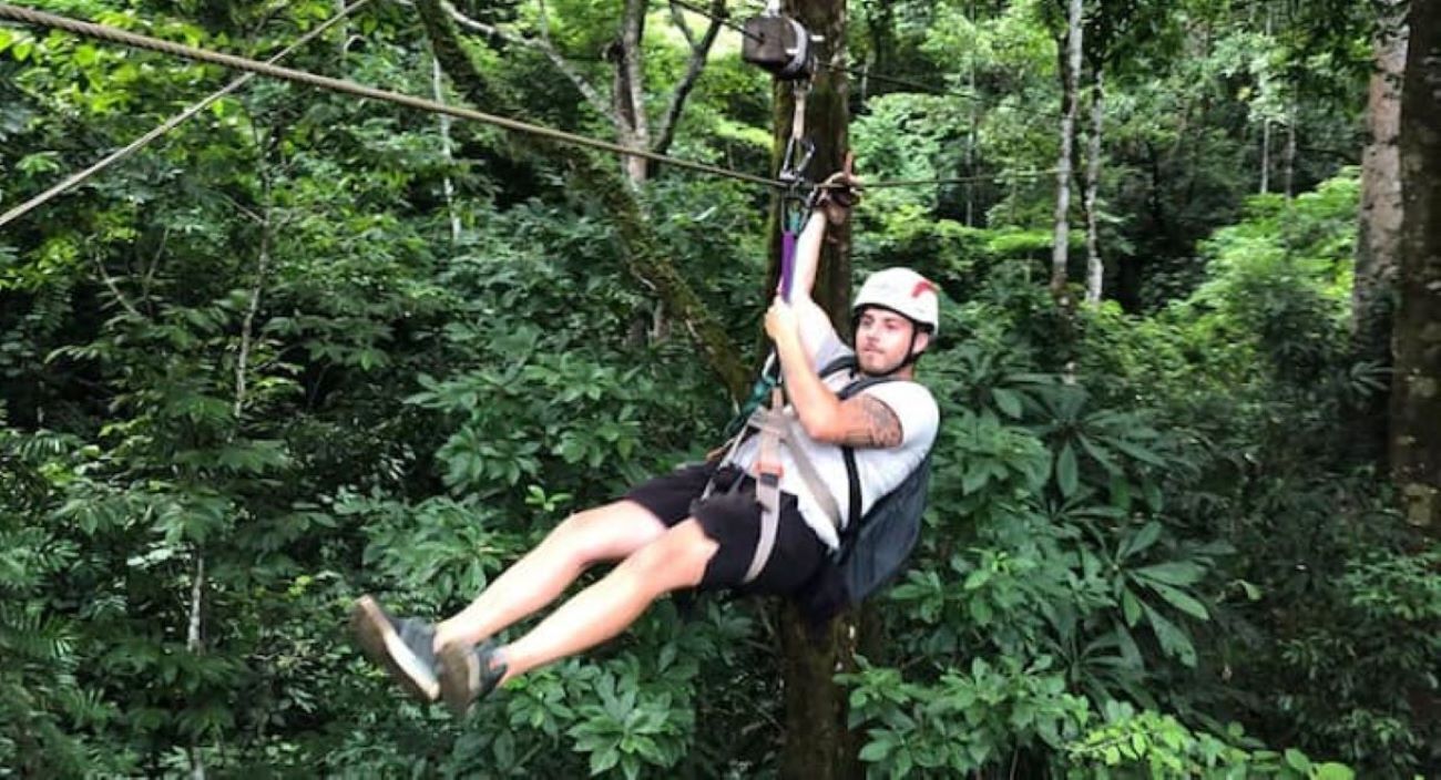 En person suser afsted i zipline gennem en tæt skov.