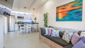 A modern kitchen with stainless steel appliances, a dining area with white chairs, and a large abstract painting on the wall. - Small romantic getaway to remind people why they fell in love (Jaco)