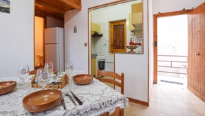 Un comedor con una mesa dispuesta para cuatro, incluyendo platos, cubiertos y copas de vino. Se observan un aparador de madera y un refrigerador al fondo.