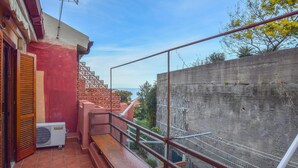 Un balcón con vista al mar, un muro de concreto y una puerta roja.