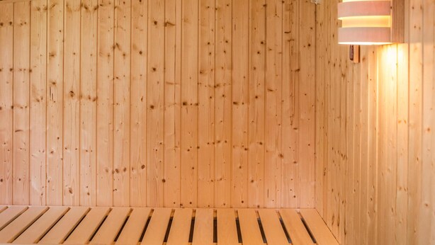 Eine Holzsauna mit Lattenbänken und einer wandmontierten Leuchte.