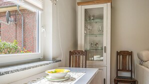 Eine Küche mit Fenster, einem Schrank mit Glastüren, zwei Holzstühlen und einem Tisch mit einer Fruchtschale.
