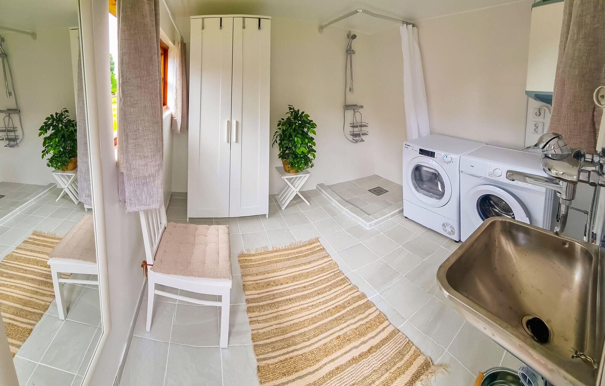 Une salle de bain moderne équipée d’un lave-linge, d’un évier et de deux plantes en pot.