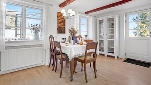 A dining area with a table set for four, wooden chairs, a chandelier, and a view of the outside through large windows.