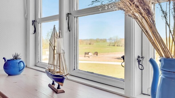 A window with a view of a grassy field and horses, a small sailboat model, and two vases on a wooden ledge.