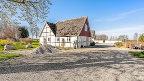 A traditional half-timbered house with a red roof, surrounded by a gravel driveway and a fenced garden area.