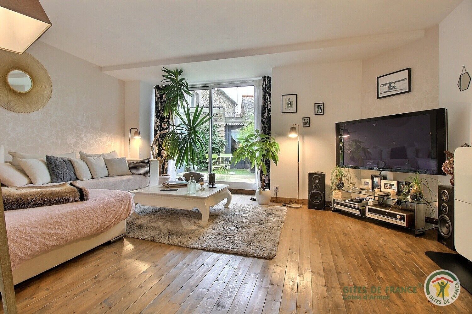 A living room with a sofa, coffee table, TV, speakers, and plants.