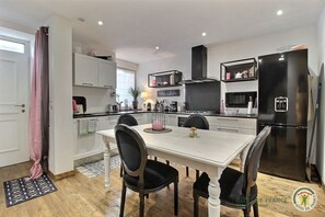 A modern kitchen with white cabinetry, a black refrigerator, and a dining area with a white table and black chairs.