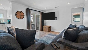 Ein modernes Wohnzimmer mit grauen Sofas, einer großen Wanduhr, einem Flachbildfernseher und einer Glastür zum Balkon.
