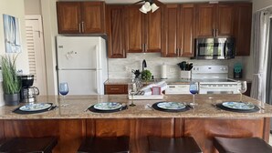 Una cocina moderna con armarios de madera, una isla central con taburetes de bar, un refrigerador, un microondas y una estufa.