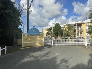 Ein verschlossenes Tor mit einem Schild 'Welcome Colony Cove', umgeben von Bäumen und Gebäuden.