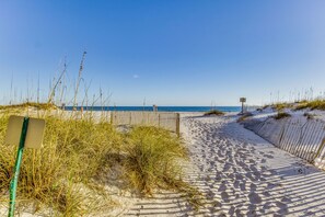 A sandy beach path with a wooden fence and a signpost.
