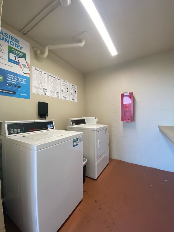 A laundry room with two front-loading washers and dryers, a fire extinguisher, and a poster with laundry tips.