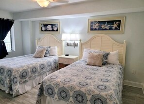 A bedroom with two beds, each with a matching headboard and pillow. There is a nightstand between the beds with a lamp on it.