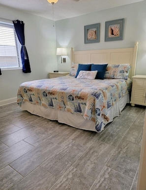 A bedroom with a bed, nightstands, a lamp, and artwork on the wall.
