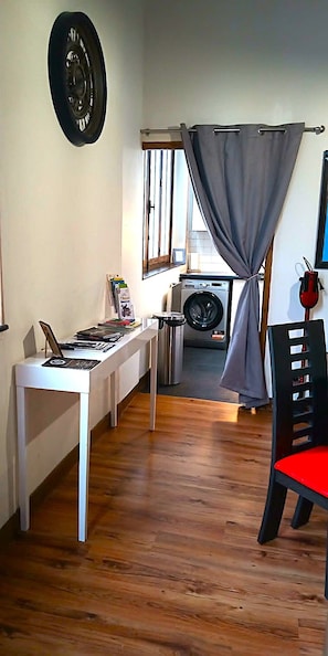 A room with a washing machine, a table with a laptop, and a chair with a red cushion.
