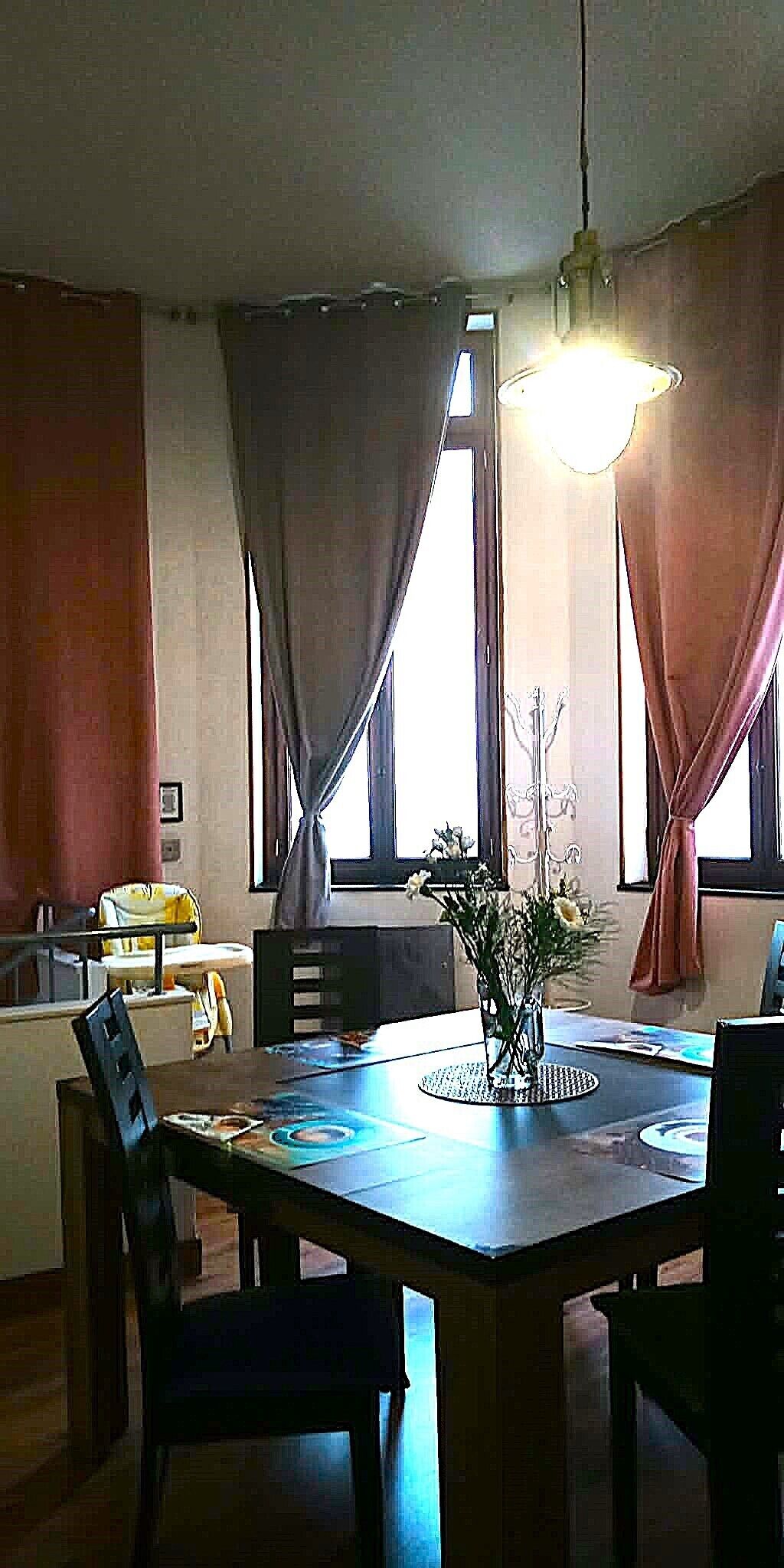 A dining area with a table, chairs, a vase with flowers, and a hanging light fixture.
