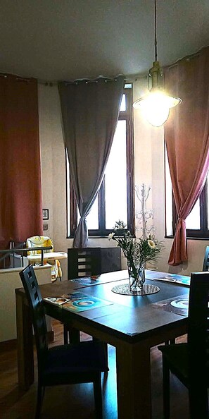 Un comedor con una mesa, sillas, un florero con flores y una lámpara colgante.