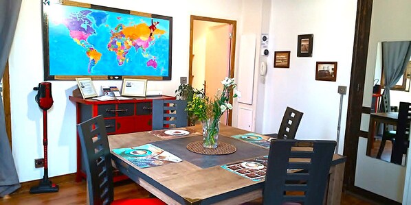 Un coin repas agrémenté d’une carte du monde, d’un aspirateur rouge, d’un vase avec des fleurs et d’une table en bois.