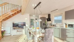Una cocina moderna con comedor, escalera de madera y un televisor grande.