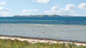 Eine Küstenlandschaft mit Sandstrand, klarem blauen Wasser und fernen grünen Hügeln.