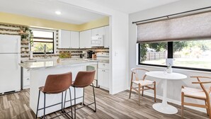 Una cocina moderna con armarios blancos, una isla central con dos taburetes, y una zona de comedor con una mesa redonda y sillas.