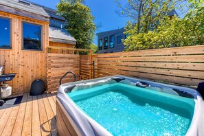 A wooden deck with a hot tub, a wooden fence, and a building with large windows.