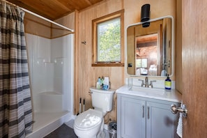 A wooden-paneled bathroom with a shower, toilet, sink, and mirror.