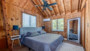 Camera da letto in una baita di legno, con un letto, una ventola a soffitto e una finestra.