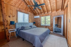 A wooden cabin bedroom with a bed, a ceiling fan, and a window.