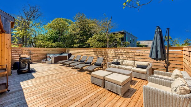 Un patio in legno con mobili in vimini, un barbecue e una zona coperta con ombrelloni.