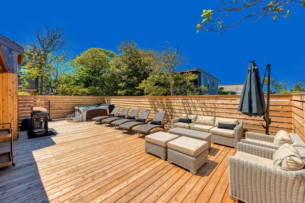 A wooden deck with wicker furniture, a grill, and a covered area with umbrellas.