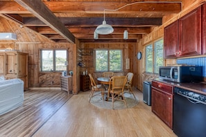 L’intérieur d’un chalet en bois comprend une table à manger, des chaises, un coin cuisine avec un four à micro-ondes et une horloge murale.