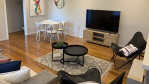 Un salon moderne comprenant un téléviseur, une table à manger avec des chaises, une table basse et un fauteuil en cuir noir.