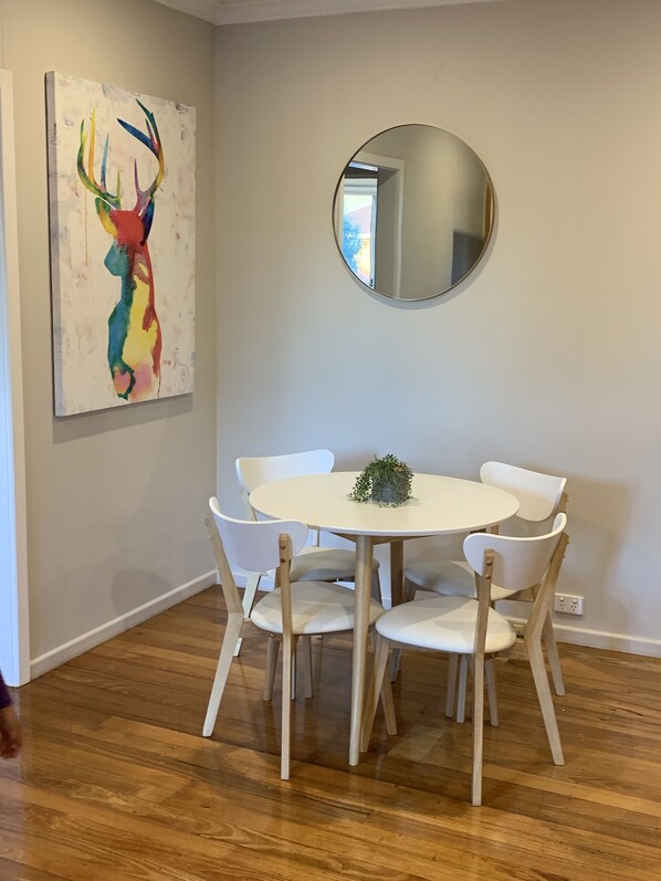 Un coin repas avec une table ronde, des chaises blanches, un miroir et un tableau abstrait aux couleurs vives accroché au mur.