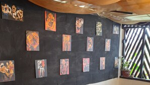Una habitación con una pared negra decorada con varias obras de arte, una mesa de madera con cuatro sillas y una ventana que da a zonas verdes.