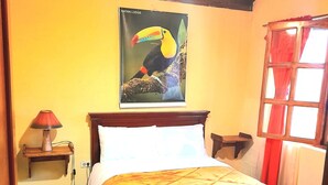 Un dormitorio con cama, mesita de noche, lámpara, un cartel en la pared y ventana con cortinas.